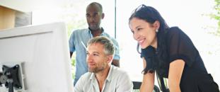 Colleagues in an office gathered around a monitor