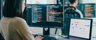 Woman sitting at a desk in an office working on a laptop and monitor
